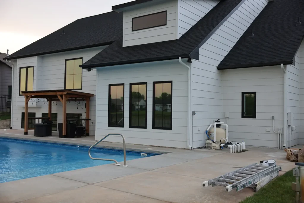Poolside house exterior with white siding, dark window trim, and painting equipment.